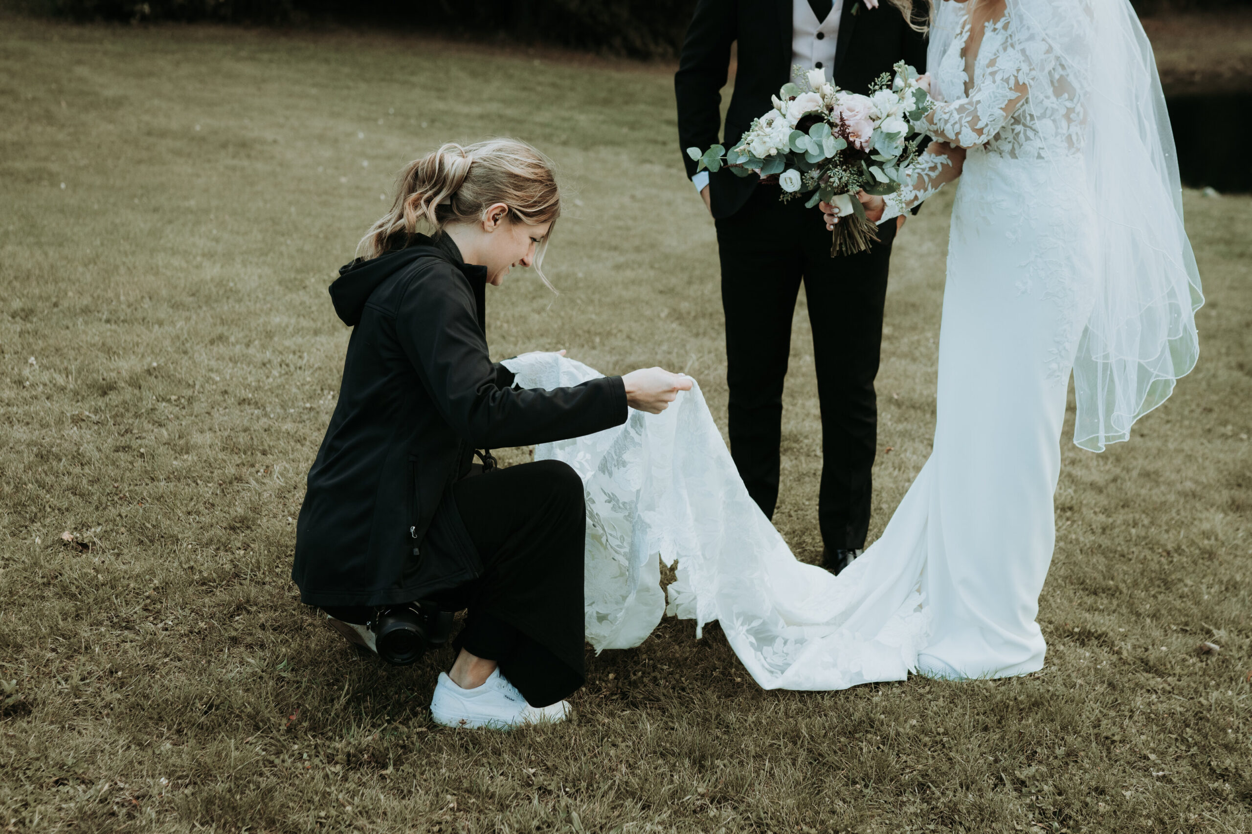 wedding photographer fixing the bride's dress for a photo